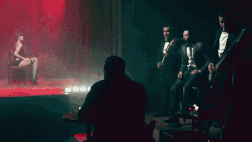 a group of men in tuxedos are sitting in front of a woman on a stage