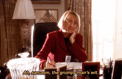 a woman is sitting at a desk and saying ah sarcasm the grumpy man 's wit