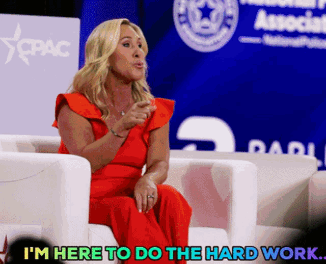 a woman in a red dress is sitting in front of a cpac logo