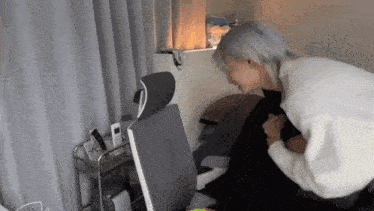 a woman in a white sweater is kneeling on a bed next to a chair .