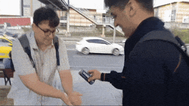 two men shaking hands with a white car driving in the background