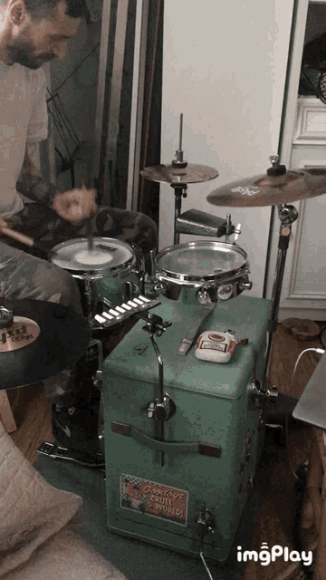 a man is playing drums in front of a green box that says custom fruit studio on it