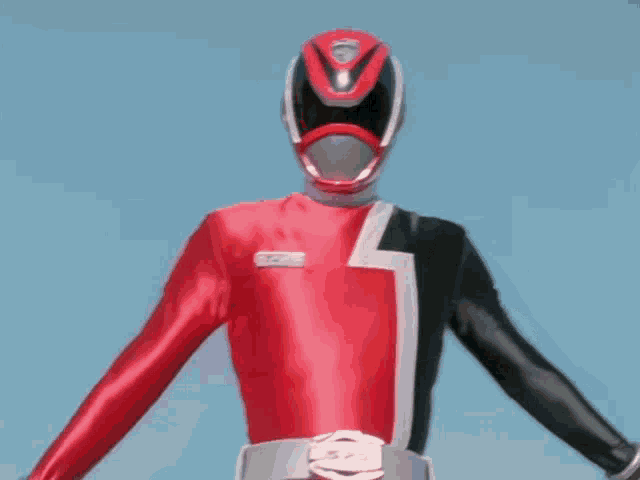 a red and black superhero with his arms outstretched against a blue sky .