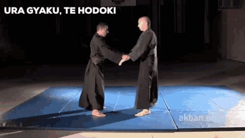 two men are standing on a blue mat with the words ura gyaku te hodoki above them
