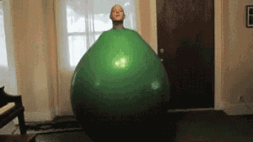 a man is standing next to a large green exercise ball in a living room .