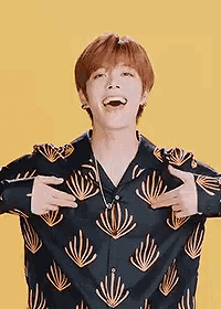 a young man wearing a black shirt with gold leaves on it is standing in front of a yellow background and laughing .