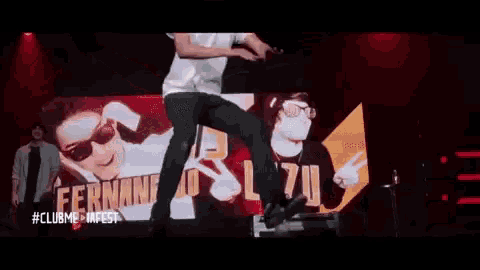 a man is dancing on a stage in front of a large screen with a picture of a man .