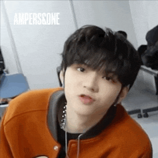 a young man wearing an orange jacket and headphones is making a face .