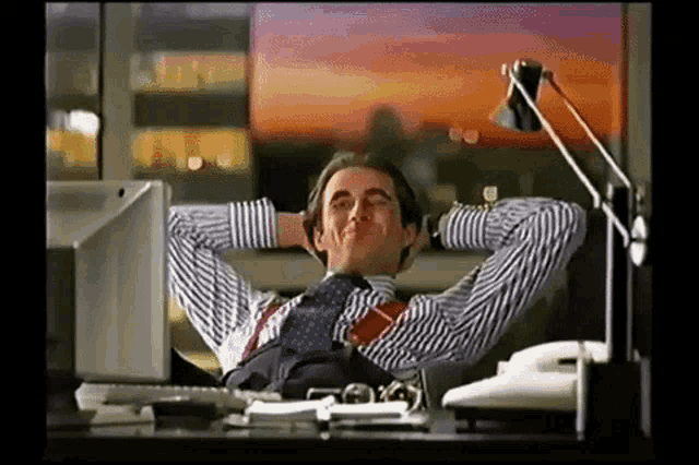 a man is sitting at a desk with his hands behind his head