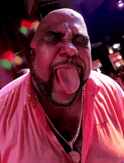 a man in a pink shirt is sticking his tongue out and the website muglife.com is in the background
