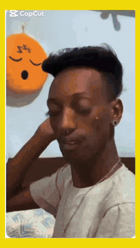 a man with his eyes closed is sitting in front of an orange pillow with a smiley face on it .