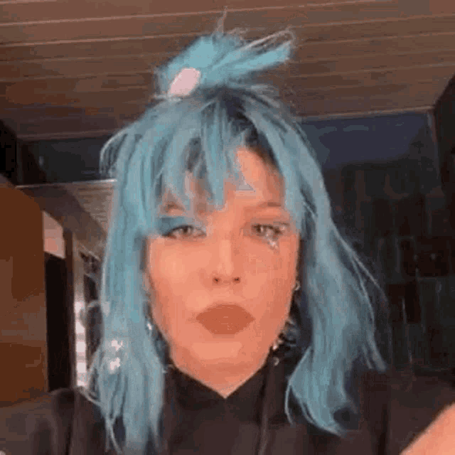 a woman with blue hair is wearing a black shirt and making a face .