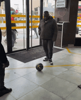a man is kicking a soccer ball in front of a sliding glass door with a sign that says no smoking