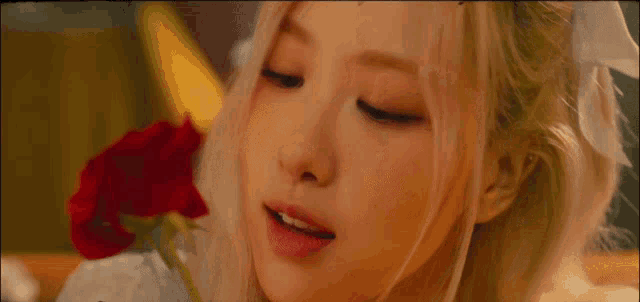 a woman with blonde hair is holding a red rose in her hand .