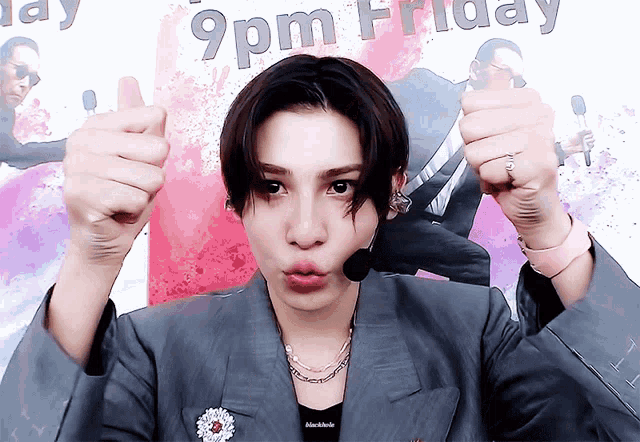 a man wearing a suit and a microphone is giving a thumbs up in front of a sign that says 9 pm friday