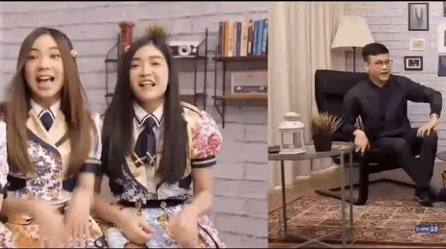 two girls are sitting next to each other in a living room with a man sitting in a chair .