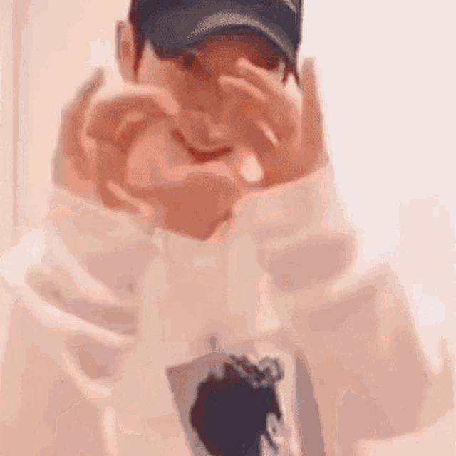a man wearing a baseball cap is making a heart with his hands .
