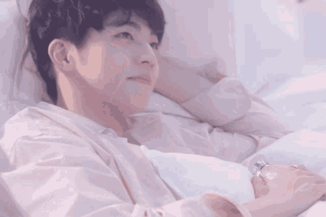 a young man in a pink shirt is laying on a bed and smiling