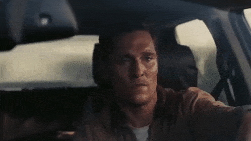 a man is driving a car and looking at the camera .