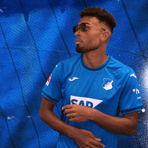 a man wearing sunglasses and a blue shirt with sap on the front