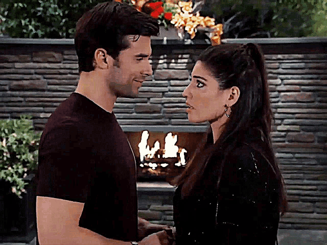 a man and woman are looking into each other 's eyes in front of a fireplace