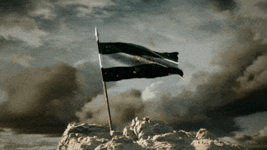 a flag on top of a rocky hill with clouds in the background