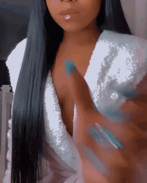 a woman with long black hair and blue nails is wearing a white sequined robe