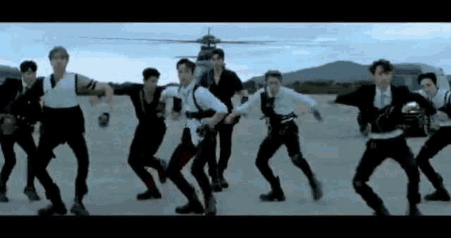 a group of young men are dancing in front of a helicopter in a field .