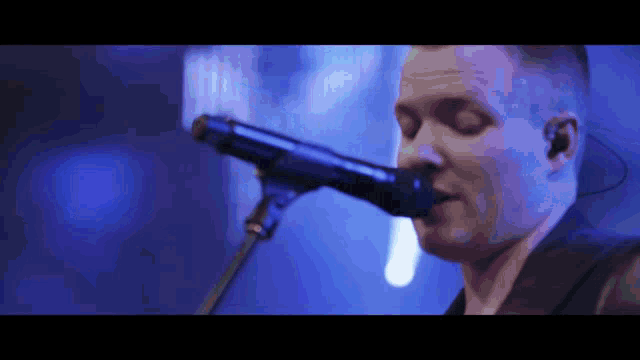 a man is singing into a microphone with a blue background