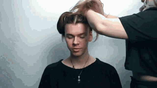 a man is getting his hair done by a woman in a black shirt and necklace .