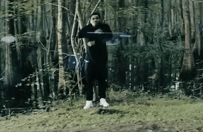 a man is standing in the middle of a forest holding a frisbee in his hand .