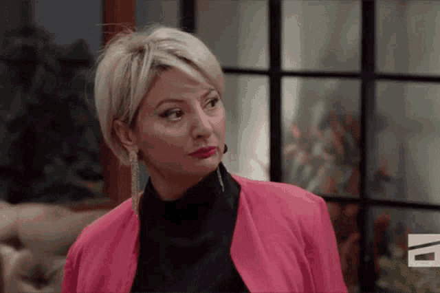 a woman wearing a pink jacket and earrings is making a funny face .