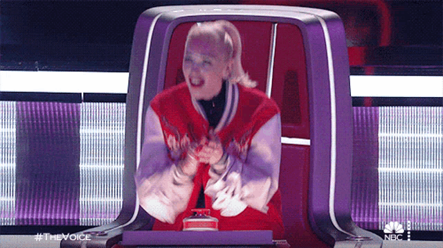 a woman in a red jacket is sitting in a chair with a nbc logo on the bottom right