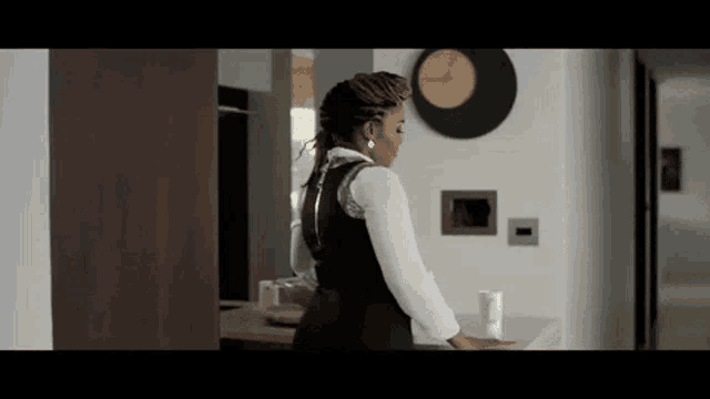 a woman is standing in a room with a clock on the wall and a table in front of her .