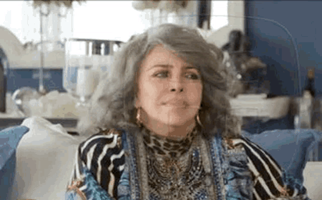 a woman with gray hair is sitting on a couch wearing a zebra print shirt and earrings .