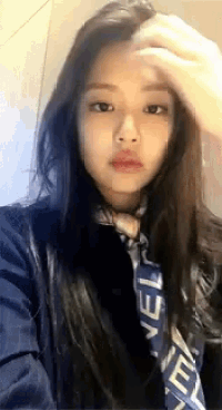 a woman wearing a scarf and a jacket is taking a selfie with her hand on her forehead .