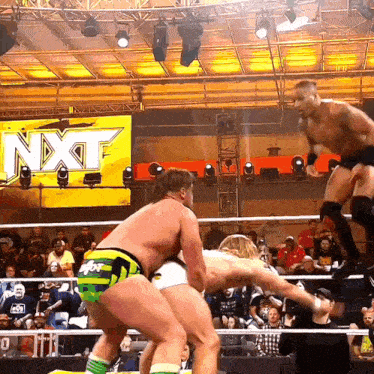 two men are wrestling in front of a sign that says nxt on it
