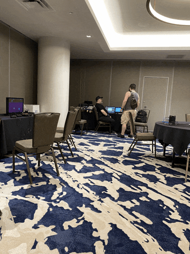 a man with a backpack stands in a room with a blue and white rug