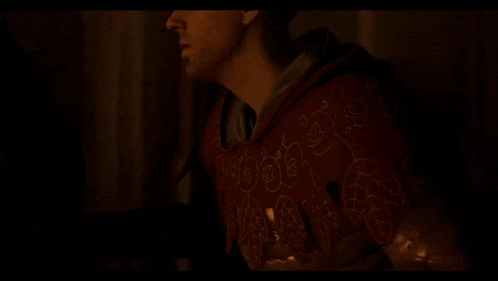 a man in a red hoodie is standing in the dark with a candle in his hand .