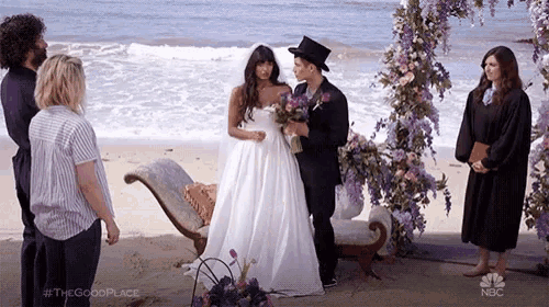 a bride and groom are getting married on a beach while a group of people watch .