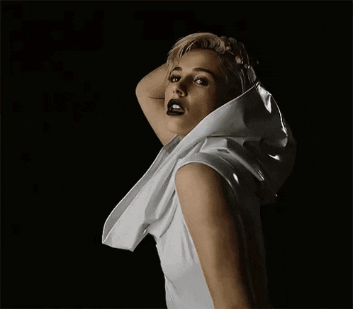 a woman in a white dress is standing in the dark with her hand on her hair .