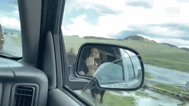 a woman driving a car with a phone in her hand and a reflection in the rear view mirror .