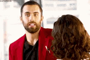 a man with a beard is talking to a woman in a red jacket .