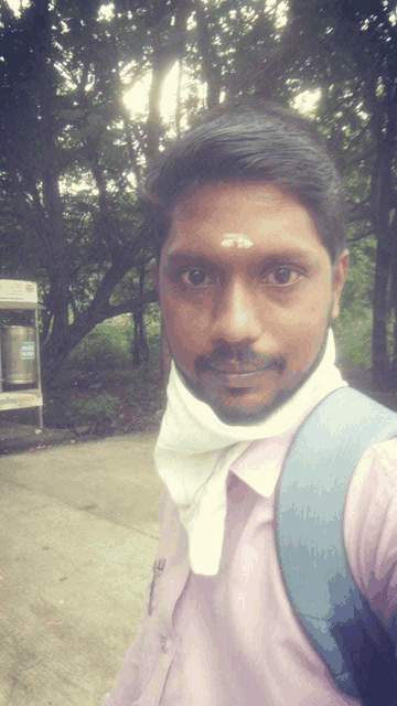 a man wearing a pink shirt and a white scarf around his neck takes a selfie