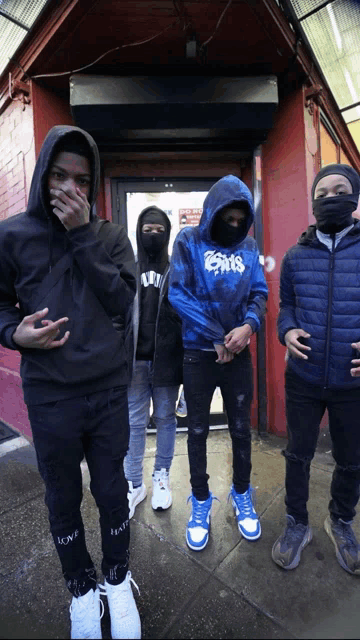 a group of young men standing in front of a red building with one wearing a hoodie that says gms