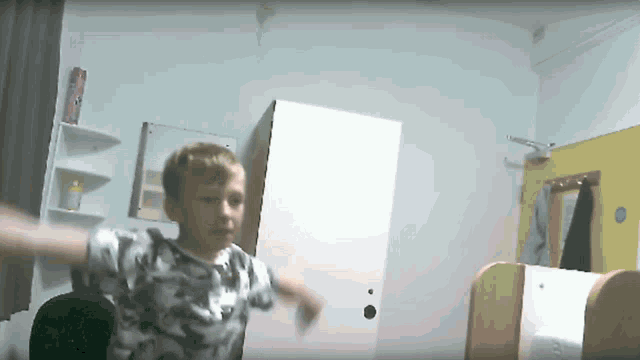 a young boy in a camouflage shirt is standing in a room