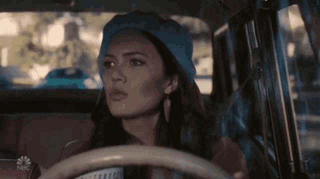 a woman wearing a blue hat is driving a car on nbc