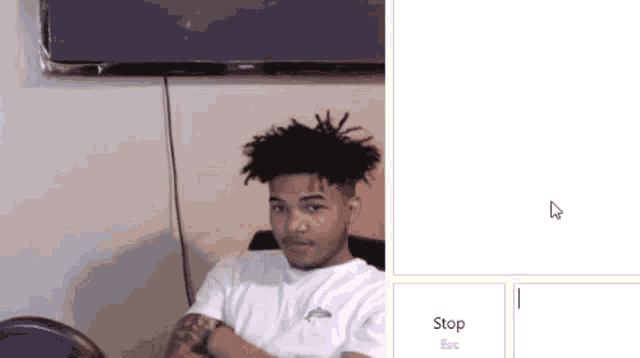 a man with dreadlocks is sitting in front of a television and a stop and esc button