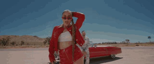 a woman in a red jacket and shorts is standing next to a red car