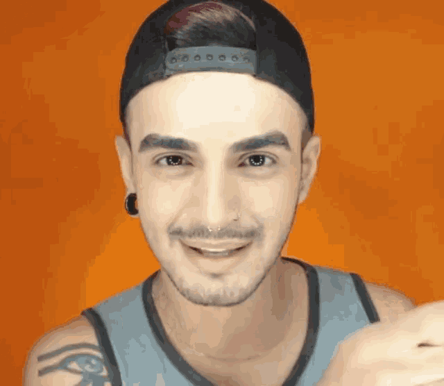 a young man wearing a baseball cap and a tank top is smiling